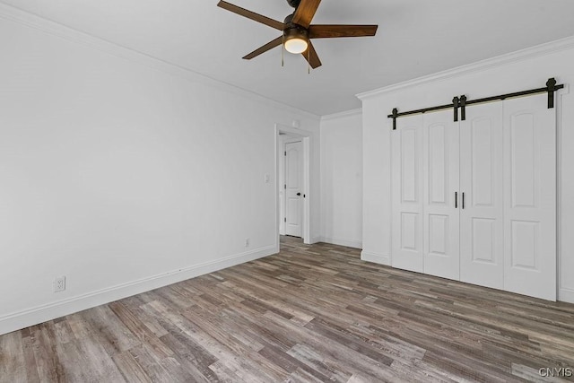 8953 Bushnell Shore Rd, Sullivan, NY 13037 - unfurnished bedroom featuring a barn door, wood finished floors, ornamental molding, ceiling fan, and a closet