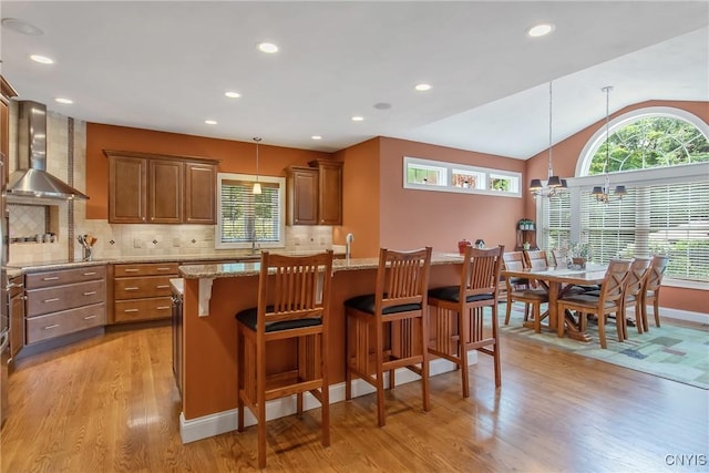 21 Donovan Dr, Oswego, NY 13126 - kitchen featuring wall chimney exhaust hood, light wood-style flooring, healthy amount of natural light, light stone countertops, and vaulted ceiling