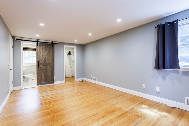 32 White Birch Cir, Chili, NY 14624 - unfurnished bedroom with a barn door, light wood finished floors, a walk in closet, recessed lighting, and connected bathroom