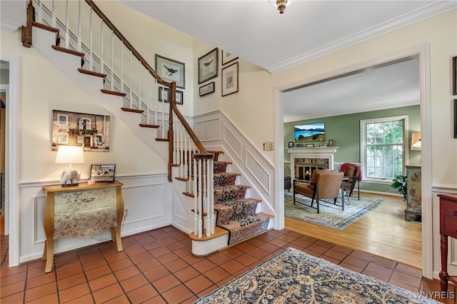 29 Cherry Tree Ln, Orchard Park, NY 14127 - stairs featuring crown molding, tile patterned flooring, a decorative wall, a glass covered fireplace, and wainscoting