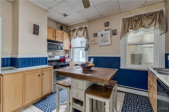 210 N James St, Wilna, NY 13619 - kitchen with stainless steel appliances, a baseboard heating unit, a wainscoted wall, light brown cabinetry, and a drop ceiling