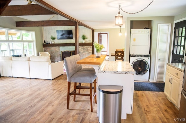 1346 Otisco Valley Rd, Otisco, NY 13110 - kitchen with stacked washing machine and dryer, light wood-style floors, a breakfast bar, a brick fireplace, and pendant lighting