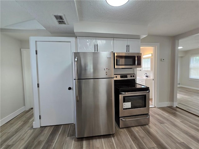 2381 Culver Rd, Irondequoit, NY 14609 - kitchen featuring stainless steel appliances, light wood-style floors, white cabinetry, and a textured ceiling