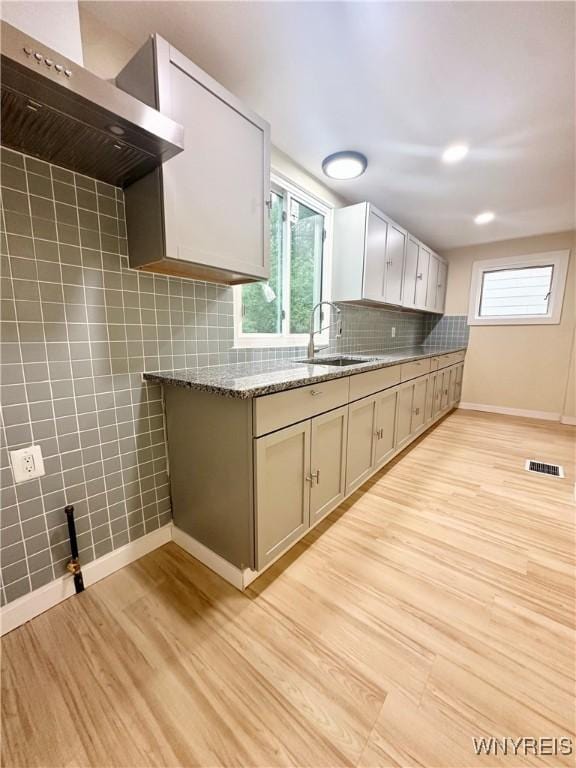 1433 Eggert Rd, Amherst, NY 14226 - kitchen with ventilation hood, light wood-style flooring, light stone counters, decorative backsplash, and tile walls