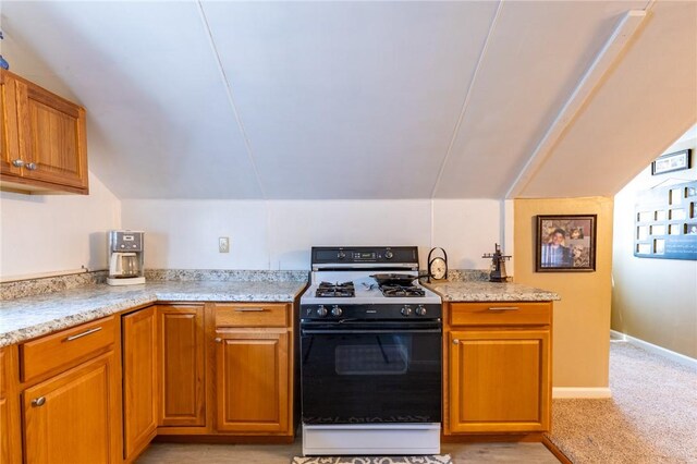 82 Barnard St, Greece, NY 14616 - kitchen featuring black gas range, vaulted ceiling, brown cabinetry, light colored carpet, and light stone counters