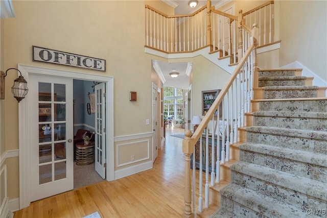 1002 Oreste St, Camillus, NY 13031 - stairway featuring wood finished floors, wainscoting, a decorative wall, a high ceiling, and french doors