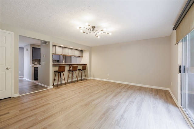 134 Jordache Ln, Ogden, NY 14559 - unfurnished living room featuring a chandelier, light wood-type flooring, and a textured ceiling