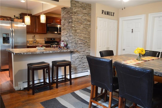 132 Main St, Unadilla, NY 13849 - kitchen featuring appliances with stainless steel finishes, a breakfast bar area, dark wood-style flooring, decorative light fixtures, and a peninsula