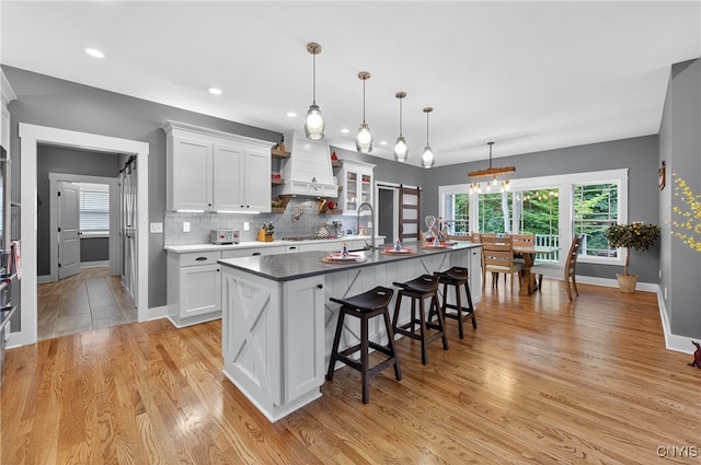 8873 Salvatore Ave, Lysander, NY 13027 - kitchen with custom exhaust hood, a breakfast bar area, light wood-style flooring, white cabinets, and a center island with sink