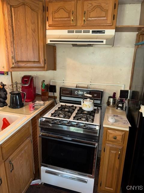 6792 Creek Rd, Lincoln, NY 13421 - kitchen featuring gas range oven, under cabinet range hood, light countertops, and brown cabinets
