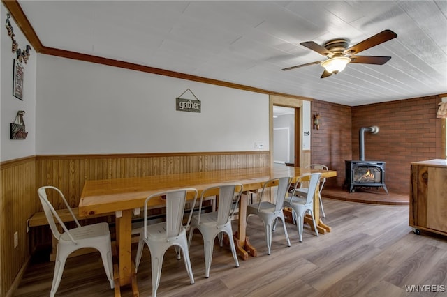 2610 Coomer Rd, Newfane, NY 14028 - dining room with a wood stove, a ceiling fan, wood finished floors, wainscoting, and crown molding
