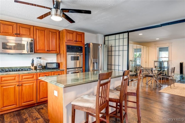 1143 Kensington Ave, Buffalo, NY 14215 - kitchen featuring stainless steel appliances, dark wood-type flooring, ceiling fan, light stone counters, and a kitchen breakfast bar