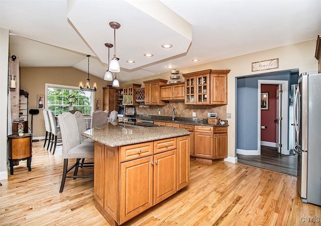 7991 Austrian Pine Cir, Pompey, NY 13104 - kitchen featuring freestanding refrigerator, brown cabinets, light wood finished floors, a kitchen breakfast bar, and decorative backsplash