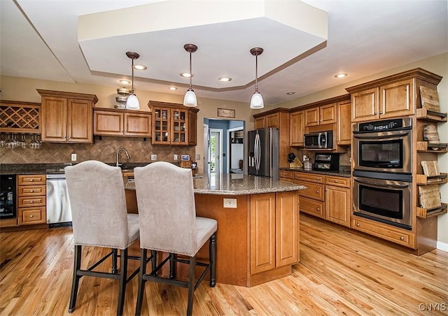 7991 Austrian Pine Cir, Pompey, NY 13104 - kitchen with appliances with stainless steel finishes, a kitchen island with sink, brown cabinetry, backsplash, and recessed lighting