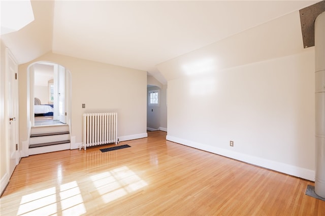 441 Claybourne Rd, Brighton, NY 14618 - spare room featuring radiator heating unit, light wood-type flooring, arched walkways, and vaulted ceiling