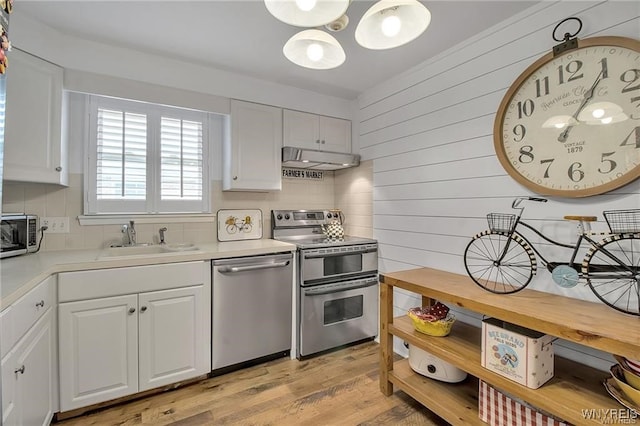 72 Old Lyme Dr Unit 3, Amherst, NY 14221 - kitchen with stainless steel appliances, under cabinet range hood, light countertops, white cabinetry, and wooden walls