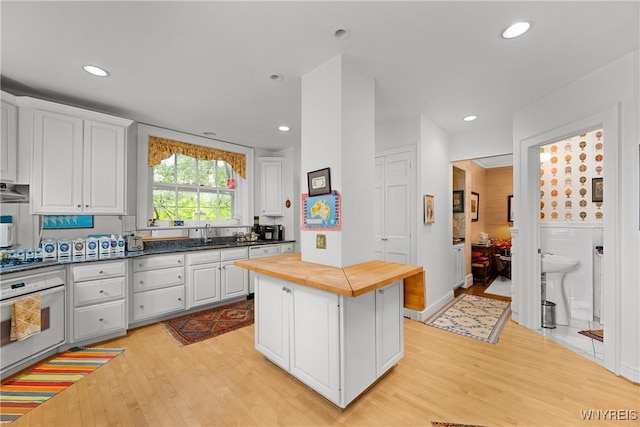 107 Oakland Pl Unit 1, Buffalo, NY 14222 - kitchen featuring oven, butcher block counters, light wood-style flooring, white cabinets, and recessed lighting