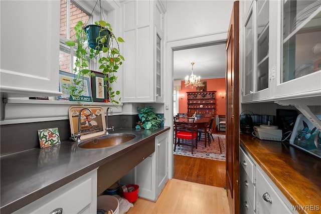 107 Oakland Pl Unit 1, Buffalo, NY 14222 - kitchen featuring light wood finished floors, white cabinets, a chandelier, glass insert cabinets, and stainless steel countertops