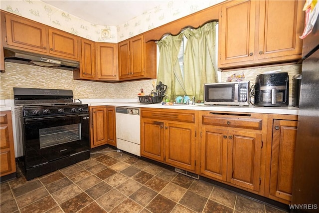 181 Ericson Ave, Buffalo, NY 14215 - kitchen with stainless steel appliances, under cabinet range hood, wallpapered walls, light countertops, and brown cabinetry