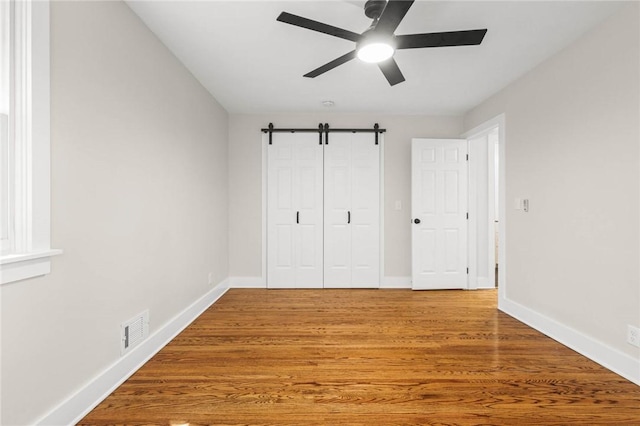 8281 E Main Rd, Leroy, NY 14482 - unfurnished bedroom featuring a barn door, a closet, light wood-style floors, and a ceiling fan