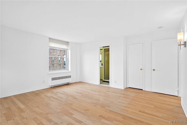 unfurnished bedroom featuring radiator, light wood-style flooring, and ensuite bathroom