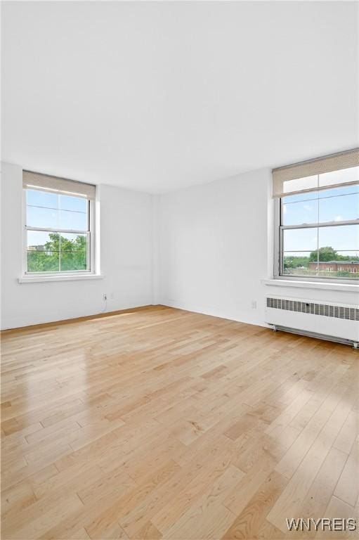 spare room with radiator heating unit, plenty of natural light, and light wood-type flooring