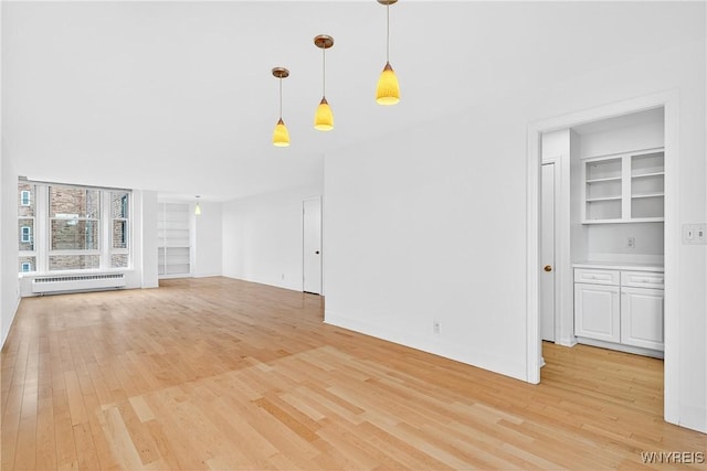 unfurnished living room with light wood finished floors, built in shelves, and radiator heating unit