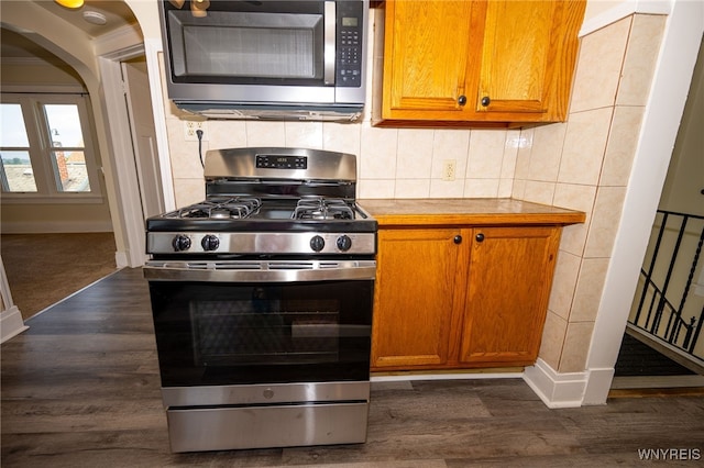 2363 Niagara St, Buffalo, NY 14207 - kitchen with stainless steel appliances, dark wood-style flooring, brown cabinets, arched walkways, and backsplash