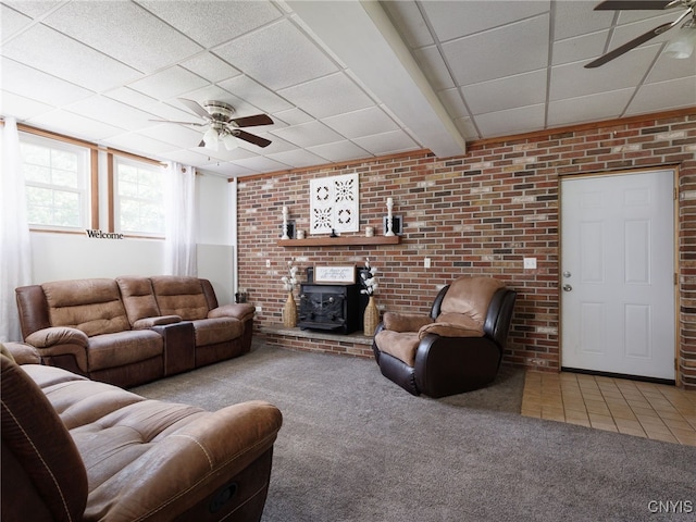 14496 Military Rd, Hounsfield, NY 13685 - carpeted living room featuring a ceiling fan, a wood stove, a paneled ceiling, and tile patterned flooring