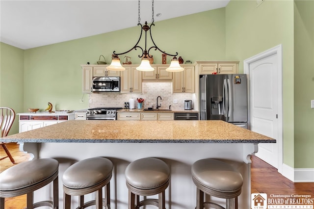 743 Legacy Dr Unit 209, Lewiston, NY 14092 - kitchen featuring stainless steel appliances, cream cabinets, a breakfast bar, wood finished floors, and tasteful backsplash