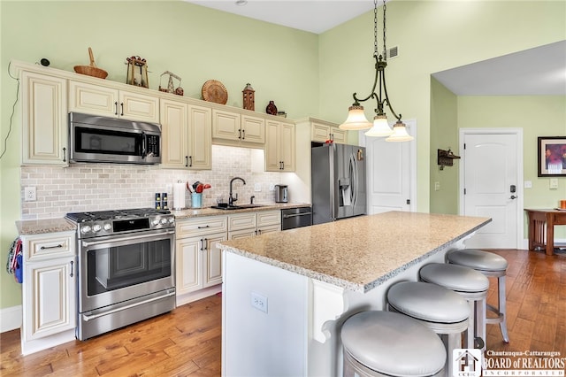 743 Legacy Dr Unit 209, Lewiston, NY 14092 - kitchen with stainless steel appliances, cream cabinets, light wood finished floors, a center island, and a high ceiling