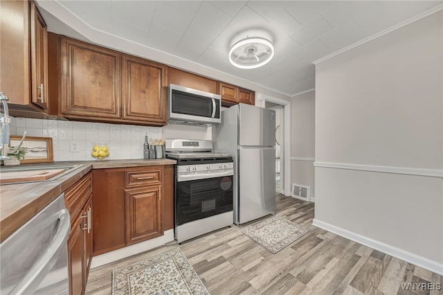 112 Southgate Rd, Cheektowaga, NY 14215 - kitchen with appliances with stainless steel finishes, light wood-style flooring, brown cabinets, crown molding, and tasteful backsplash