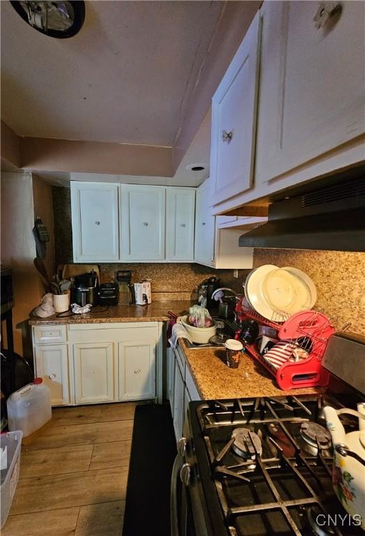 1125 Adams St, Utica, NY 13501 - kitchen featuring gas range, white cabinets, light wood-style floors, tasteful backsplash, and under cabinet range hood