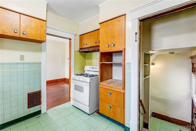 2239 Willow Ave, Niagara Falls, NY 14305 - kitchen with white gas stove, under cabinet range hood, brown cabinets, light tile patterned flooring, and crown molding