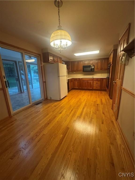 124 N Way, Camillus, NY 13031 - kitchen featuring freestanding refrigerator, black microwave, brown cabinets, light wood finished floors, and hanging light fixtures