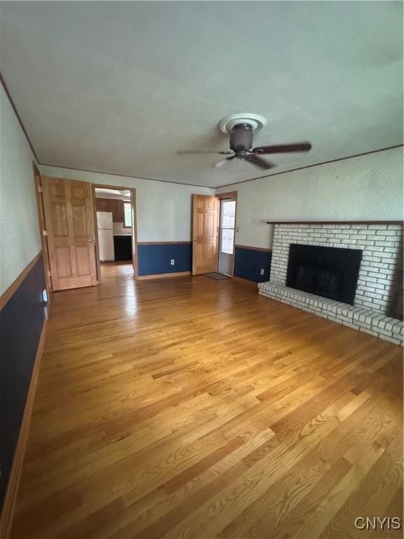 124 N Way, Camillus, NY 13031 - unfurnished living room with light wood-type flooring, ceiling fan, a fireplace, and a wainscoted wall