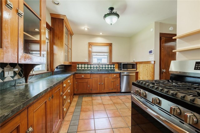 1043 Genesee Park Blvd, Rochester, NY 14619 - kitchen with appliances with stainless steel finishes, brown cabinets, dark countertops, light tile patterned floors, and glass insert cabinets