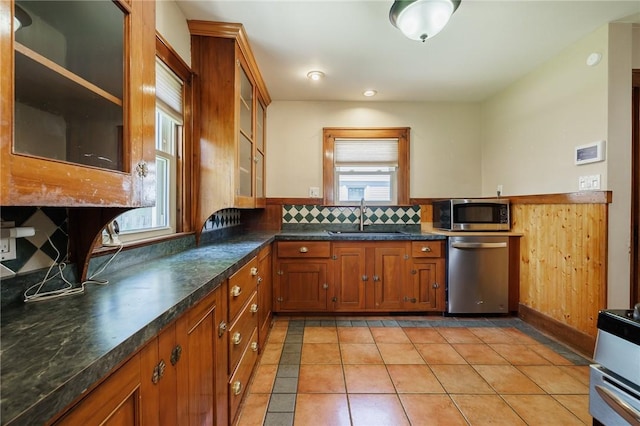 1043 Genesee Park Blvd, Rochester, NY 14619 - kitchen featuring stainless steel appliances, brown cabinetry, glass insert cabinets, light tile patterned flooring, and a wainscoted wall