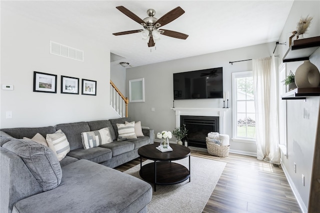 2023 Rainbow Ln, Lima, NY 14485 - living area with wood finished floors, a ceiling fan, a fireplace with flush hearth, and stairs