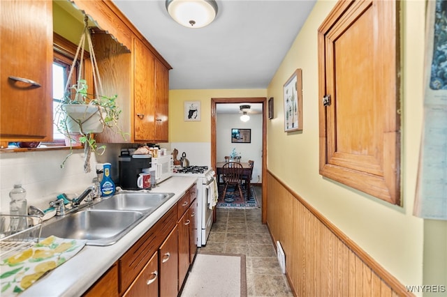 235 Wagner Ave, Cheektowaga, NY 14212 - kitchen featuring white gas range oven, brown cabinets, light countertops, and a wainscoted wall