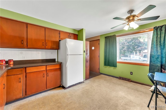 85 Pacific Ave, Lackawanna, NY 14218 - kitchen with freestanding refrigerator, brown cabinetry, dark countertops, ceiling fan, and backsplash