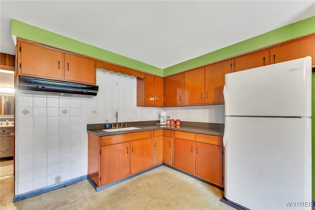 85 Pacific Ave, Lackawanna, NY 14218 - kitchen with freestanding refrigerator, dark countertops, under cabinet range hood, brown cabinets, and backsplash