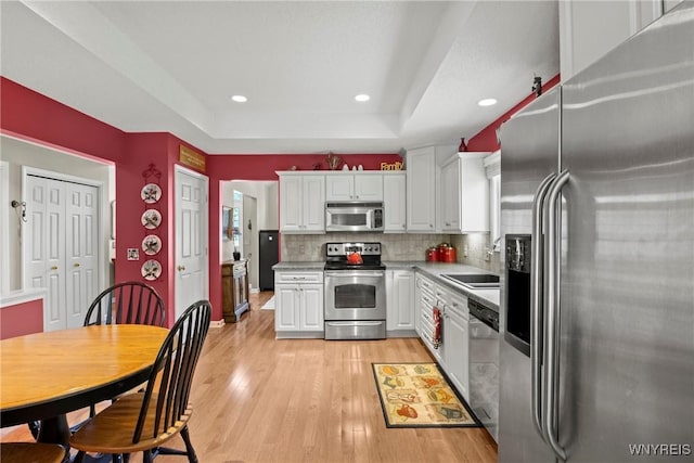6 Fair Woods Dr, Amherst, NY 14221 - kitchen featuring stainless steel appliances, light wood finished floors, white cabinets, a tray ceiling, and tasteful backsplash