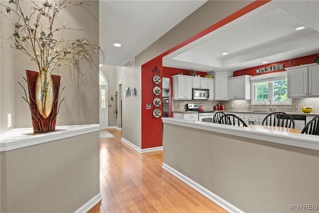 6 Fair Woods Dr, Amherst, NY 14221 - kitchen with recessed lighting, tasteful backsplash, stainless steel appliances, light wood-type flooring, and a raised ceiling