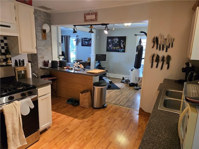 262 E 3rd St, Corning City, NY 14830 - kitchen with stainless steel gas stove, dark countertops, light wood-style flooring, white cabinetry, and exhaust hood