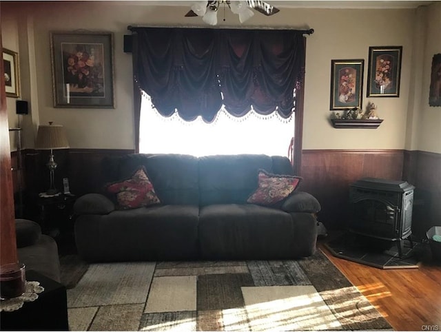 living room with ceiling fan, a wood stove, and wood-type flooring