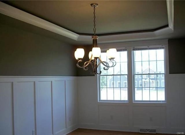 unfurnished dining area featuring a wealth of natural light, a tray ceiling, hardwood / wood-style flooring, and an inviting chandelier