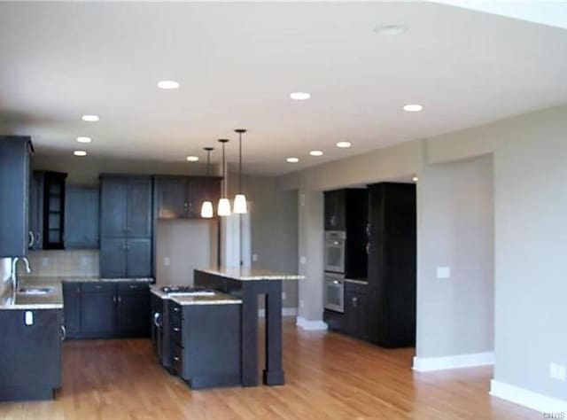 kitchen with decorative light fixtures, light hardwood / wood-style flooring, a center island, double oven, and sink