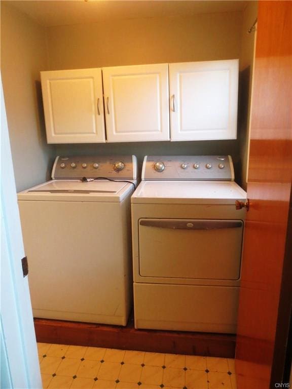 clothes washing area featuring light tile flooring, washing machine and dryer, and cabinets