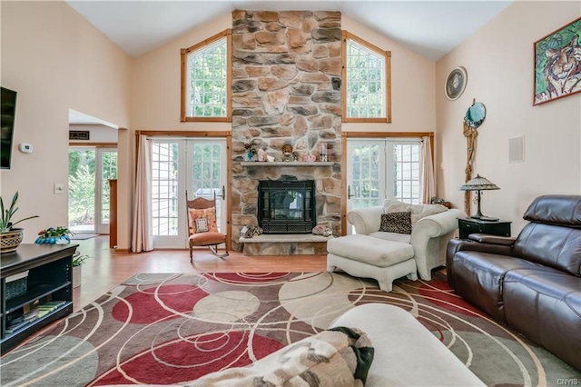 living room featuring high vaulted ceiling, light wood-type flooring, french doors, and a stone fireplace